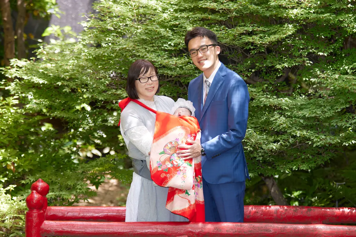 緑を背に、赤ちゃんを抱いて並ぶお父さんとお母さん