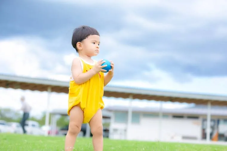 黄色い服を着た小さな子どもが芝生の上でボールを持っている