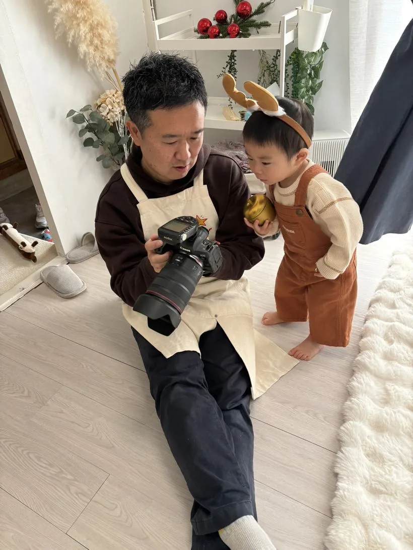 スタジオの床に座ってカメラを構える赤田佳史と、そばに立って手元をのぞきこむ小さな男の子