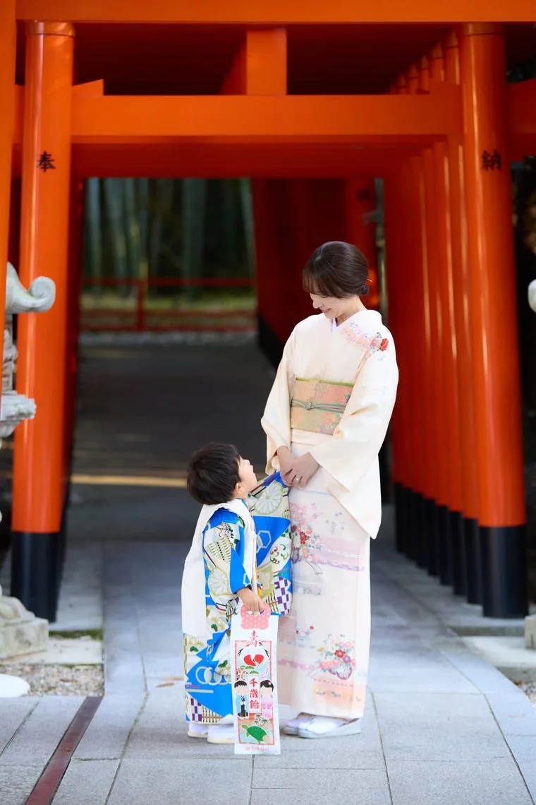鳥居の下で、着物姿のお母さんと手をつなぐ女の子