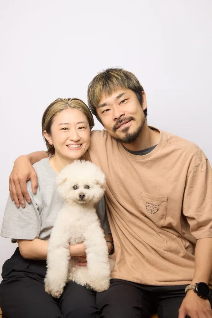 スタジオで白いプードルを抱いて笑う夫婦