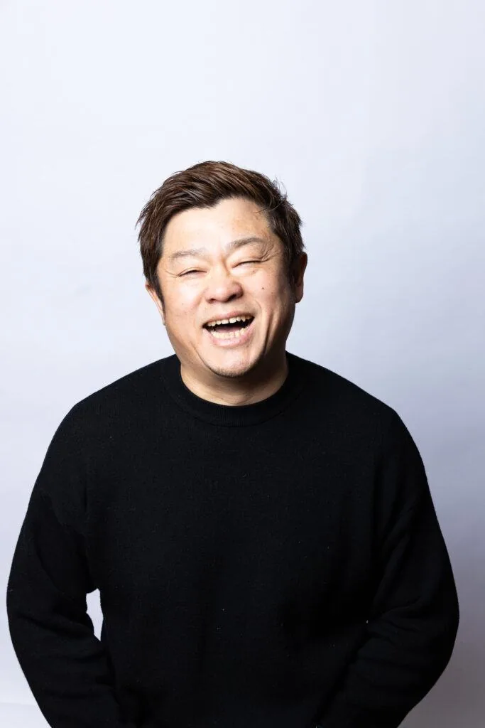 暗い背景の前で、口を開けて笑っている男性のプロフィール写真