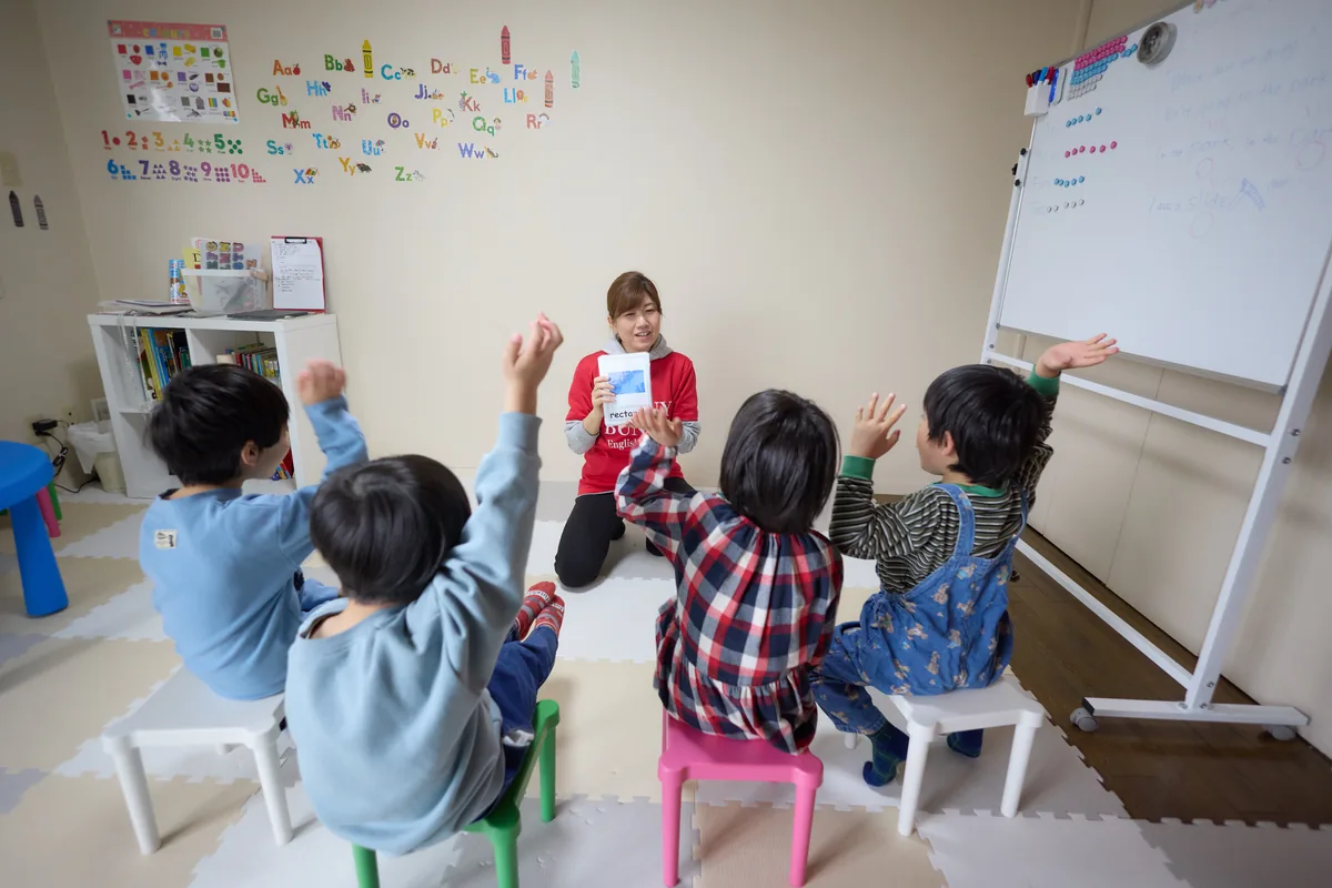 教室で、先生の話に手を挙げてこたえる子どもたち